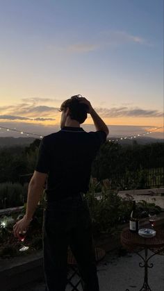 a man standing on top of a roof next to a lush green field at sunset