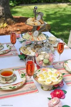 a table topped with plates and cups filled with food next to wine glasses on top of a white table cloth