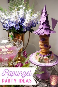 a table topped with cakes and desserts next to a vase filled with purple flowers