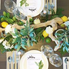 the table is set with white plates, silverware and greenery as well as lemons