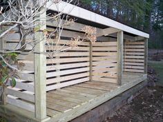 a wooden bench sitting on top of a wooden deck next to a forest filled with trees