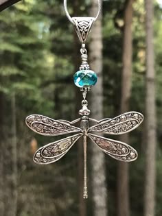 a dragonfly is hanging from a tree branch in the woods with a blue crystal bead