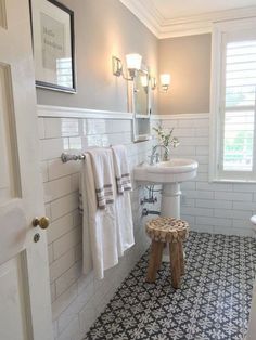 a white bathroom with black and white tile flooring on the walls, along with a wooden stool