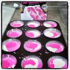 cupcake tins with pink and white icing in them on a baking tray