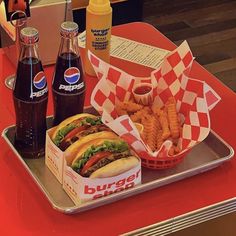 a tray that has some food on it and two sodas in front of it