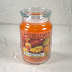 a glass jar filled with orange and peach flavored candles on top of a white surface