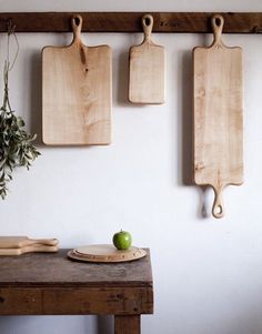 three cutting boards mounted to the wall above a wooden table with an apple on it