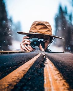 a person taking a photo on the road with a camera in their hand and wearing a hat