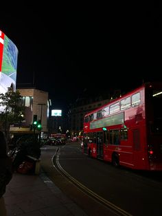 a red double decker bus driving down a street at night