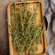 a wooden cutting board topped with lots of green herbs next to a checkered cloth