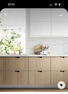 a kitchen counter with wooden drawers and white cabinets in front of a window that has plants on it