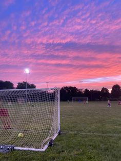 a soccer goal with the sun setting in the background and people playing on the field