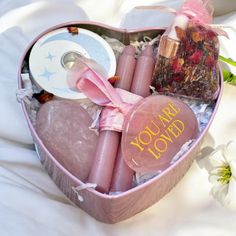 a pink heart shaped box filled with candles and other personal care items next to flowers