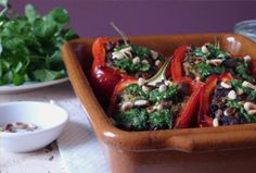 a brown bowl filled with stuffed peppers covered in toppings next to some greens and other vegetables