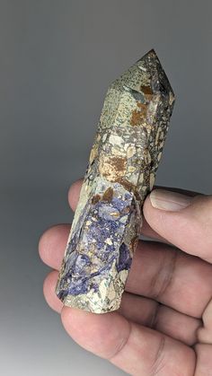 a hand holding a piece of rock with blue and yellow paint on it's surface