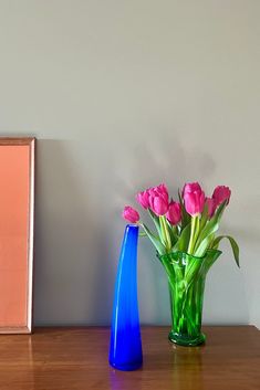 pink tulips in a blue vase on a table next to a framed photograph