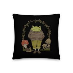 a black pillow with an image of a frog wearing a sweater and mushrooms on it