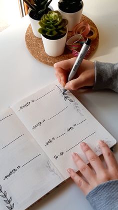 a person writing on a notebook with succulents and plants in the background