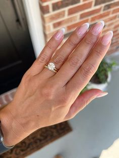 a woman's hand holding a diamond ring in front of a brick wall and potted plant