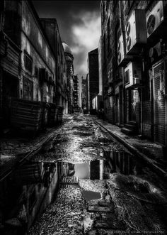 a black and white photo of an old city street with puddles in the middle