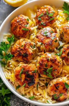 a bowl filled with pasta and meatballs on top of a table next to lemon wedges