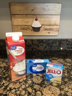 three boxes of jello sitting on top of a counter next to a cupcake