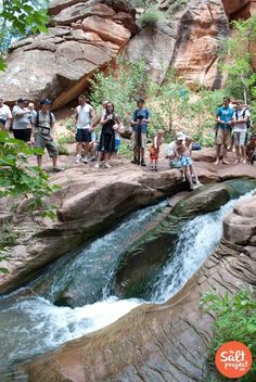 people are standing on the edge of a cliff and looking at a river running through it