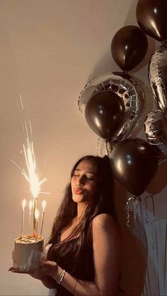 a woman holding a cake with sparklers in her hand and some balloons behind her