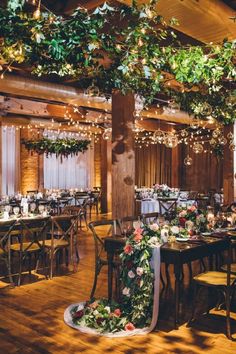 an indoor venue with tables and chairs covered in flowers, greenery and hanging lights