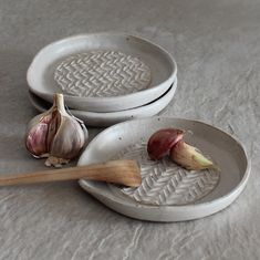 three white plates with garlic on them and a wooden spoon in the middle one has an onion