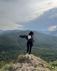 a woman standing on top of a mountain with her arms outstretched