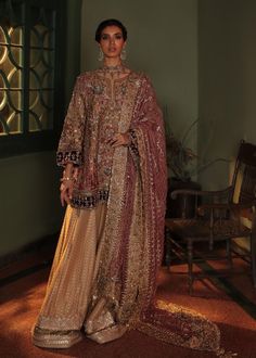 a woman standing in a room wearing a brown and gold outfit with an elaborate shawl