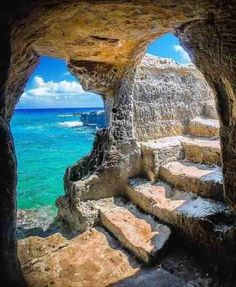 an arch in the side of a rock formation with water and rocks below it, looking out into the ocean