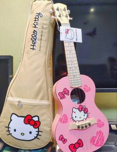 a pink guitar with hello kitty decals on it next to a case for an electric guitar