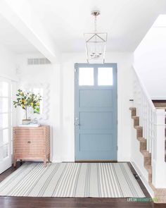 a blue door in a white room with stairs and rugs on the floor next to it