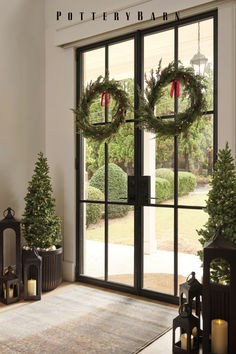 two wreaths are on the windowsill in front of christmas trees and lanterns with lit candles