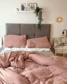 an unmade bed with pink sheets and pillows in a white room next to a plant