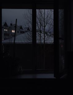 an open window in a dark room with snow on the roof and bare trees outside