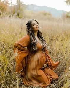 a pregnant woman sitting in tall grass with her arms behind her back, looking up at the sky