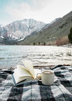 an open book sitting on top of a blanket next to a lake