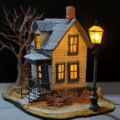 a small house with a light on in front of a tree and lamp post at night