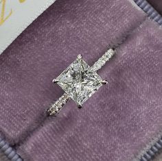 a princess cut diamond ring on top of a purple blanket