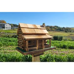 a wooden bird house on top of a post in the middle of a grassy field