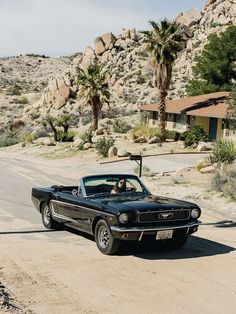 an old black car is parked on the side of the road in front of some rocks