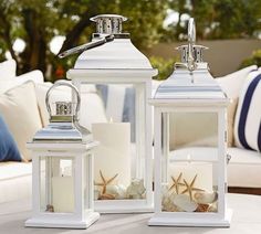 two white lanterns sitting on top of a table with seashells and starfish