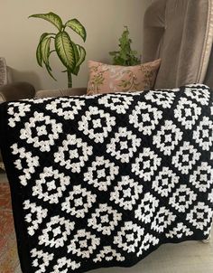 a black and white crocheted blanket sitting on top of a chair next to a potted plant