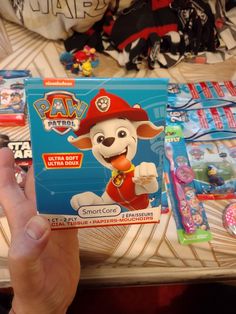 a person holding up a package of paw patrol toys in front of some other items