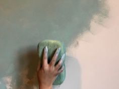 a person's hand holding a green sponge on top of a white painted wall