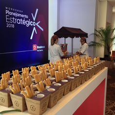 two people standing at a table with some food in baskets on it and an event sign behind them