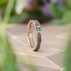 a close up of a wedding ring with a green stone in the center on a tile floor